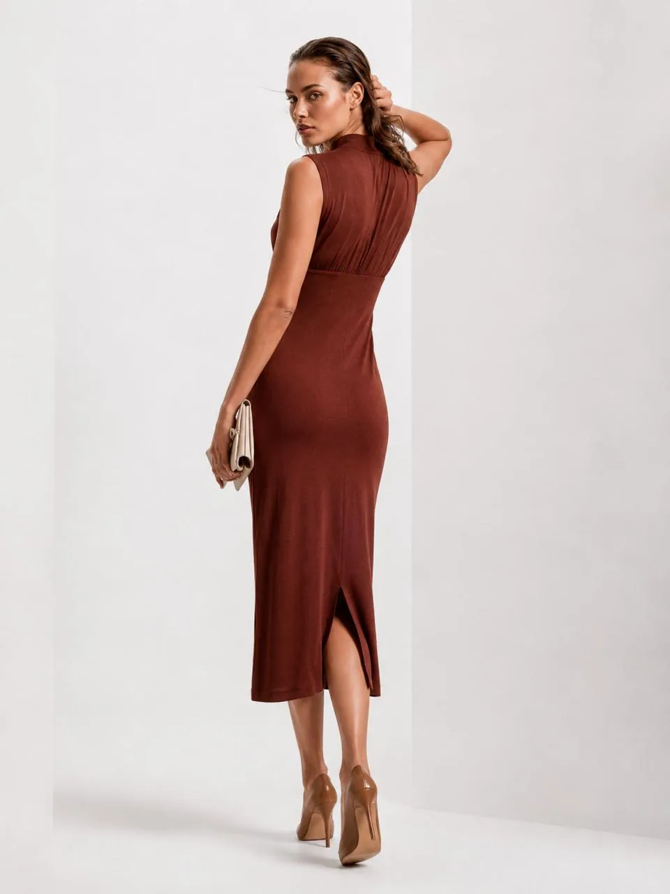 Back view with a clutch — the ruched back bodice and centre-back hem slit of the terracotta midi.