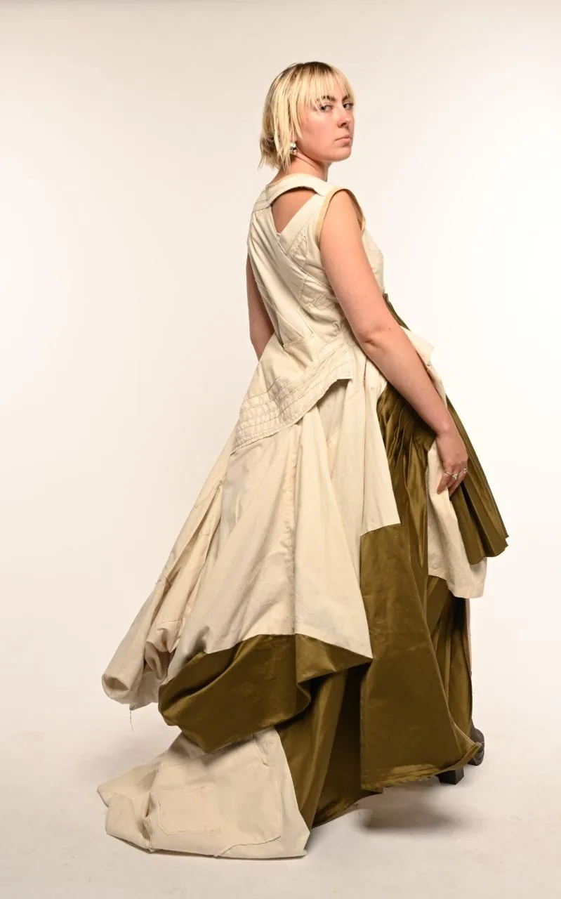 Three-quarter back view in motion — the olive pleated train swinging out to reveal the patched cream panels and cut-out back.