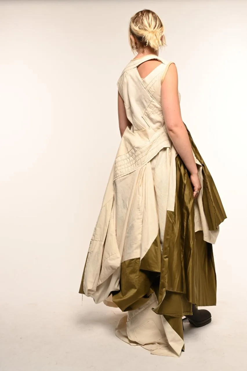 Side view — the model holding out the olive pleated panel beside the cream cotton gown, the cut-out back bodice visible.