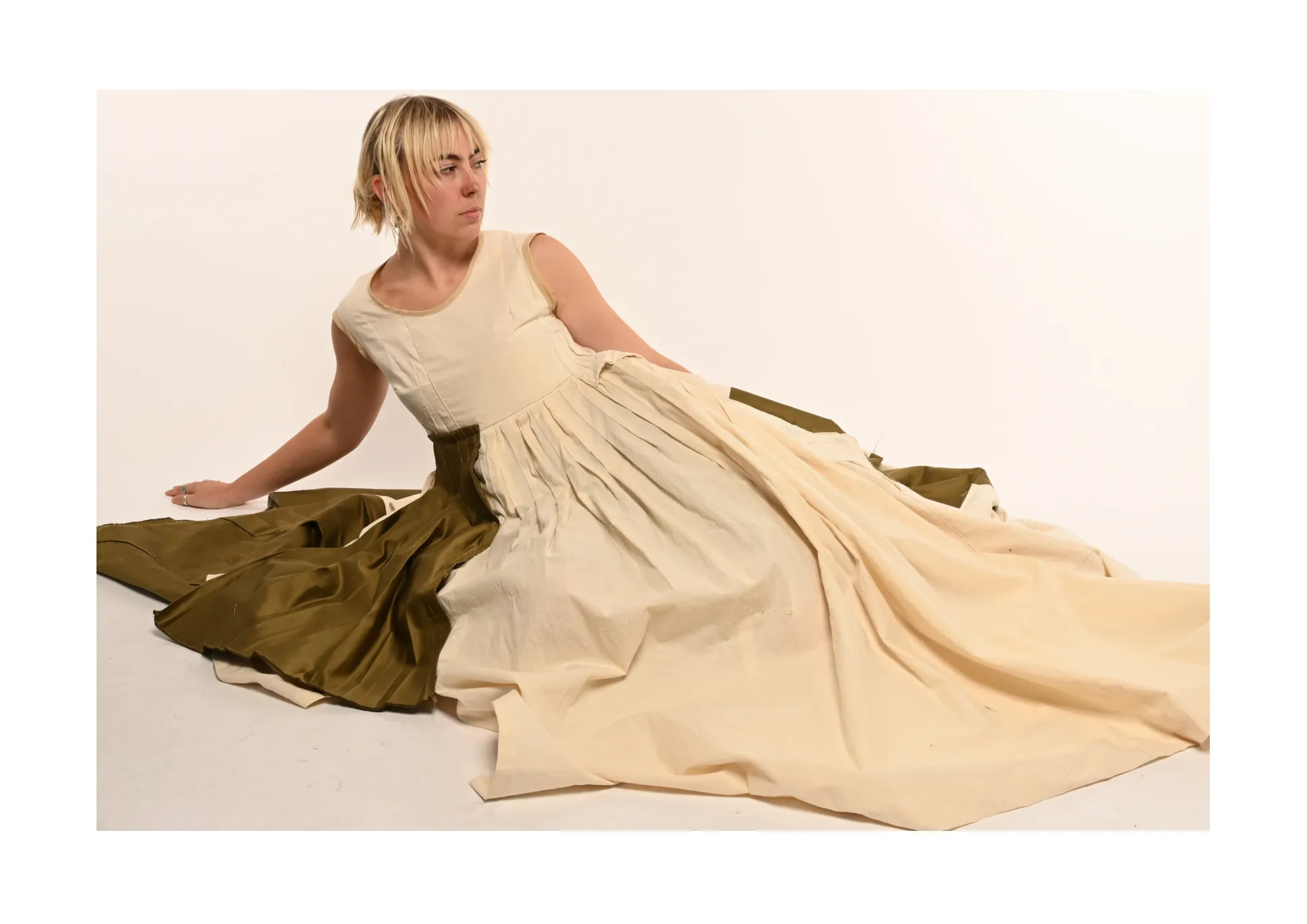 Full-length spread — the model reclining in the cream gown with the olive train spread across the floor.
