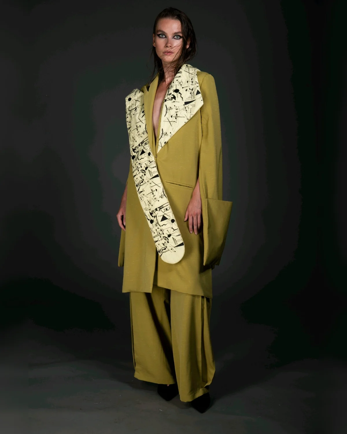 Subjective Surrealism cover — the model facing front in the oversized dusted-olive coat and wide trousers, the hand-doodled surrealist embroidery panel crossing the body.