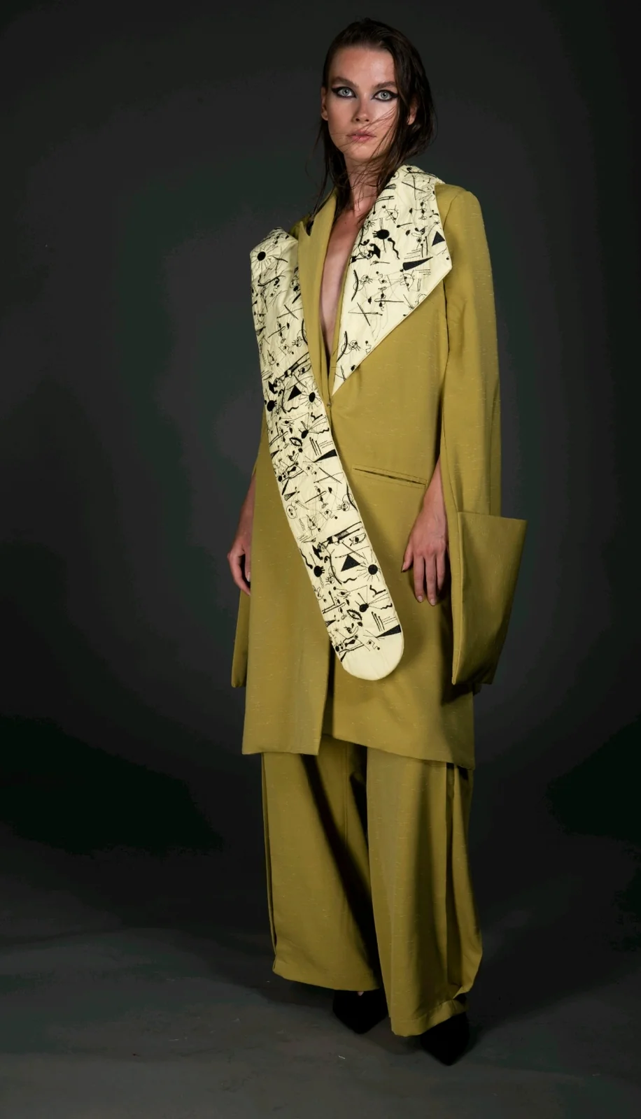 Subjective Surrealism cover — the model facing front in the oversized dusted-olive coat and wide trousers, the hand-doodled surrealist embroidery panel crossing the body.